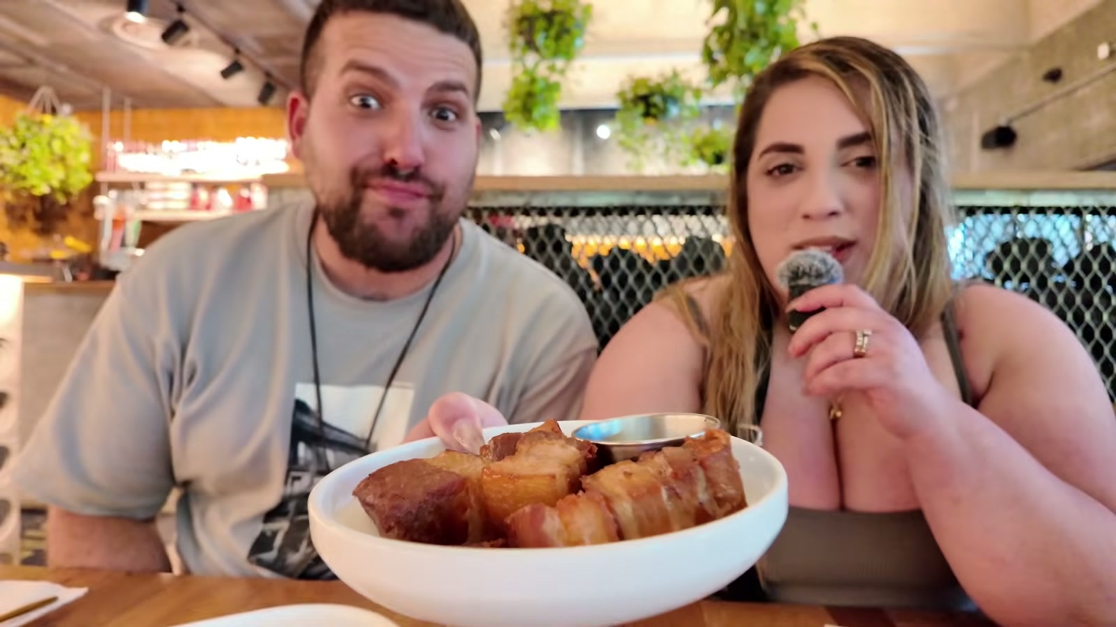 Gerardo y Diana sentados a la mesa de Dando La Brasa, con el bol de chicharrones con guasacaca en primer plano.