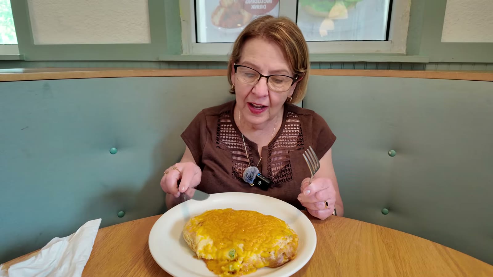 Mami Lupe, cubiertos en mano, frente a su Western Omelette con cheddar gratinado, en un reservado verde menta de The Original Pancake House.